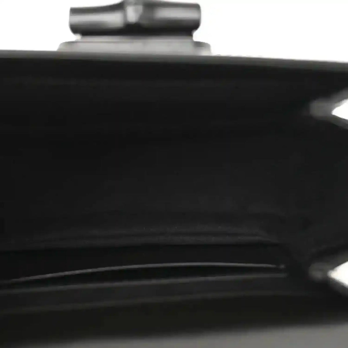 Black handbag close-up of a seam and metallic hardware detail near top.
