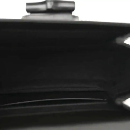 Black handbag close-up of a seam and metallic hardware detail near top.