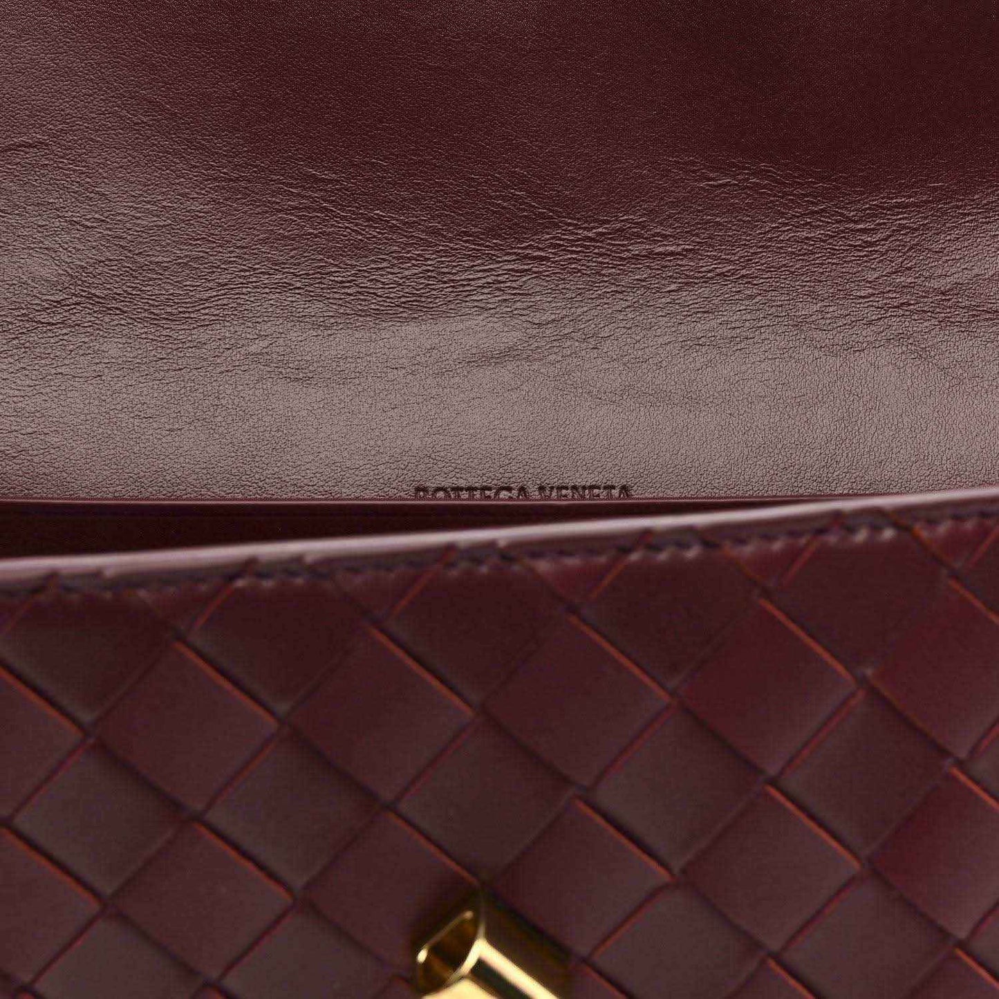 Burgundy intrecciato clutch close-up with embossed logo and gold hardware corner