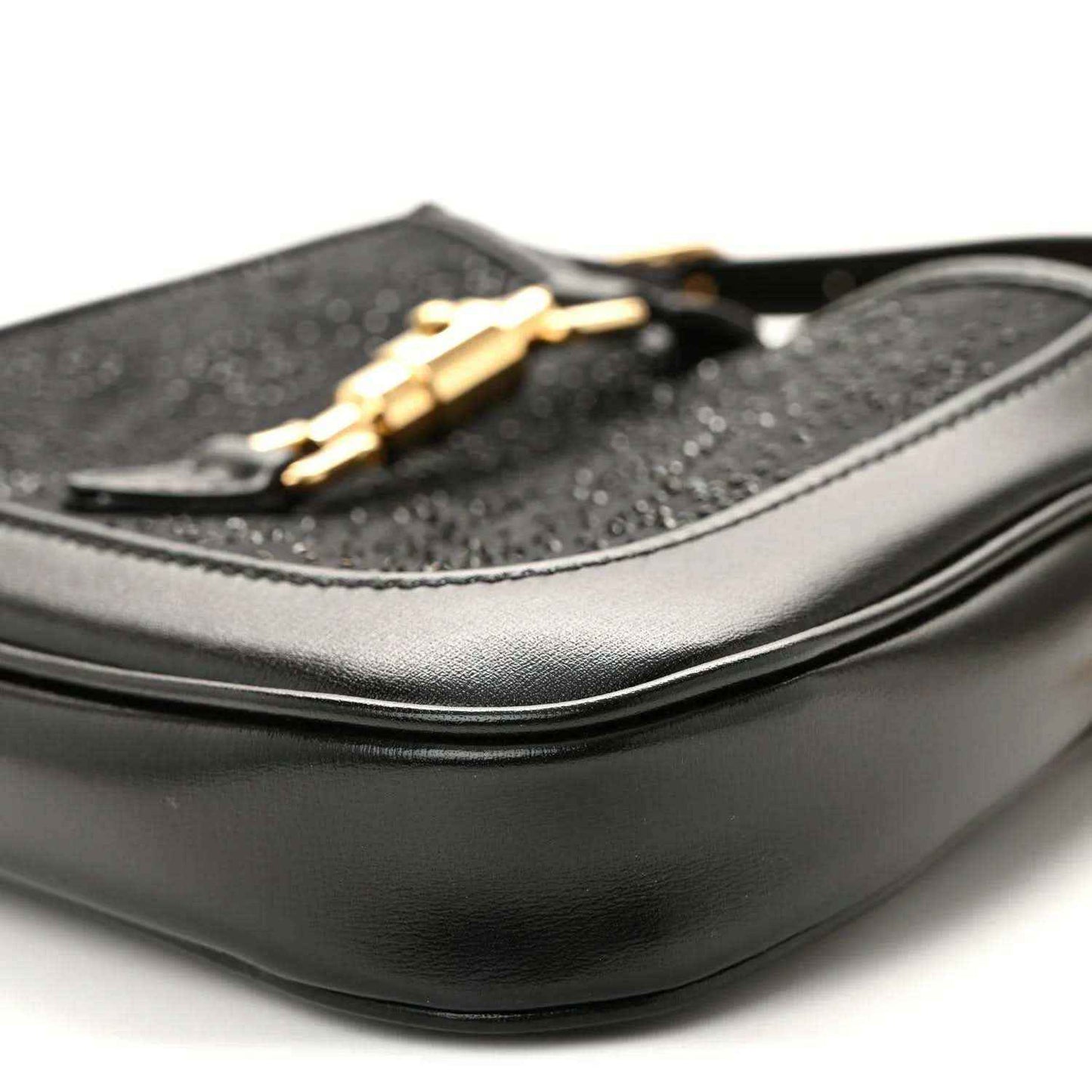 Close-up of black hobo bag side with curved leather panel and gold chain detail.