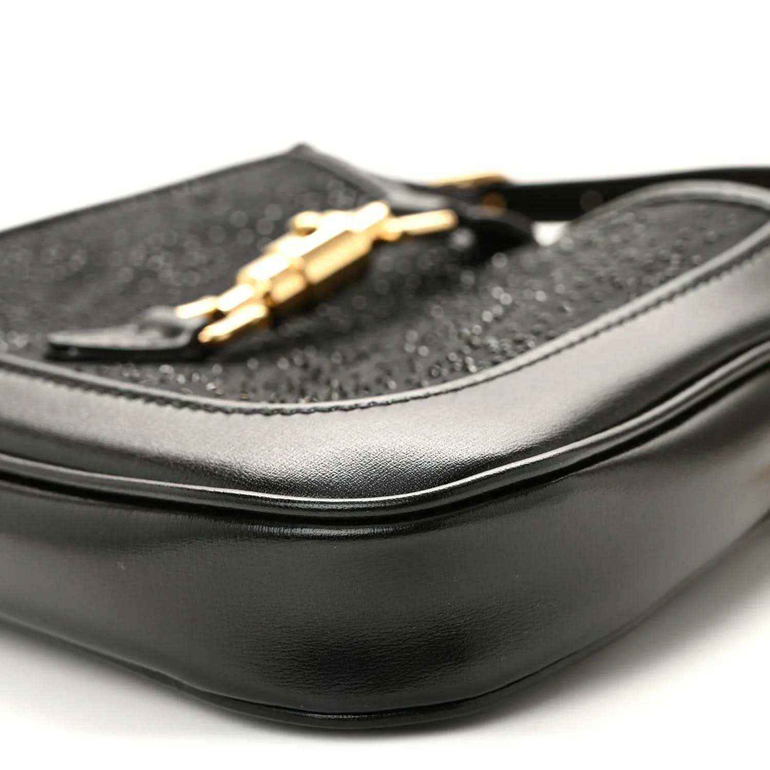 Close-up of black hobo bag side with curved leather panel and gold chain detail.