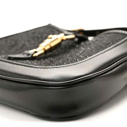 Close-up of black hobo bag side with curved leather panel and gold chain detail.