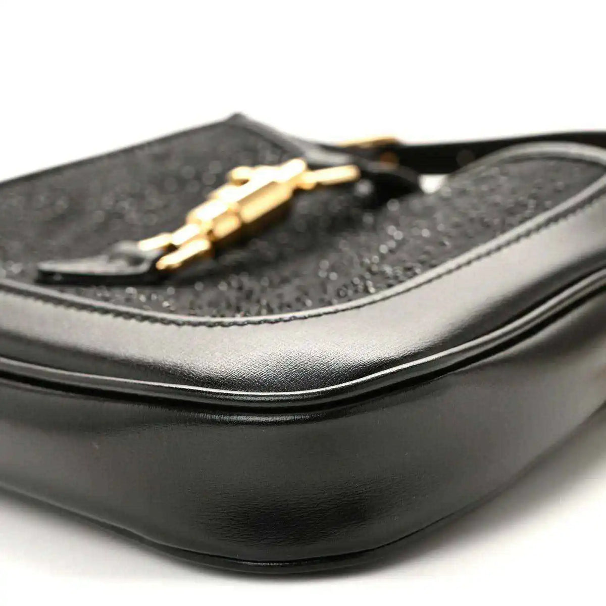 Close-up of black hobo bag side with curved leather panel and gold chain detail.