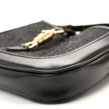 Close-up of black hobo bag side with curved leather panel and gold chain detail.