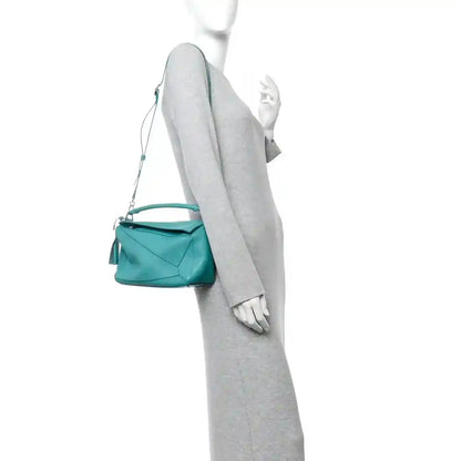 Teal-blue small Puzzle bag carried with long crossbody strap; front view on model.