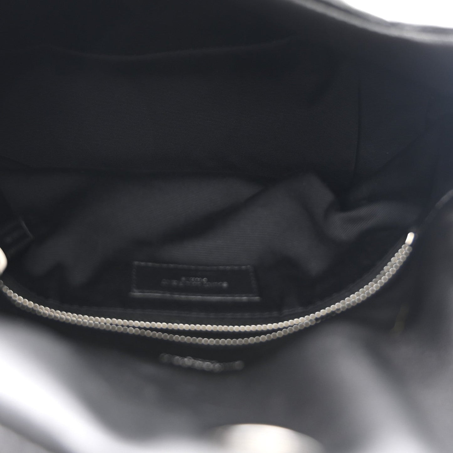 Black satin-lined interior of small satchel with zipper opening and silver chain detail.