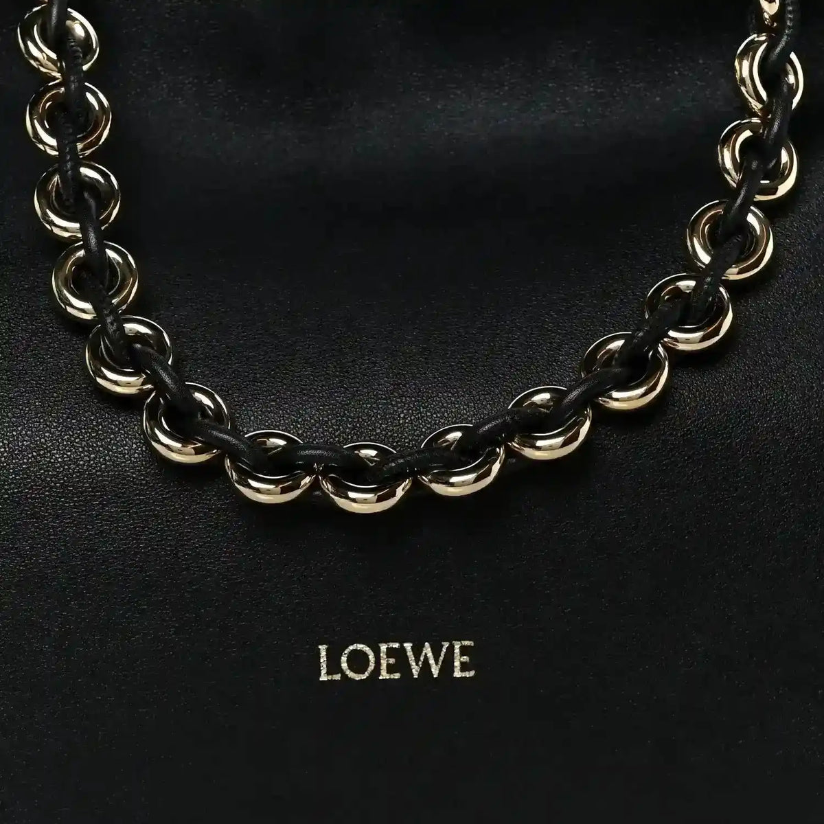 Black leather clutch with chunky gold-tone chain strap and centered LOEWE logo.