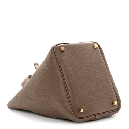 Taupe leather bucket bag with triangular flap and gold snap hardware.
