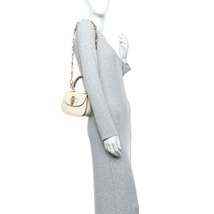 White mini handbag worn on shoulder with short gold chain strap and bamboo handle