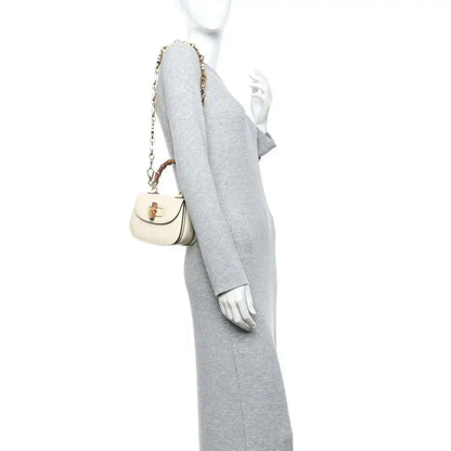 White mini handbag worn on shoulder with short gold chain strap and bamboo handle