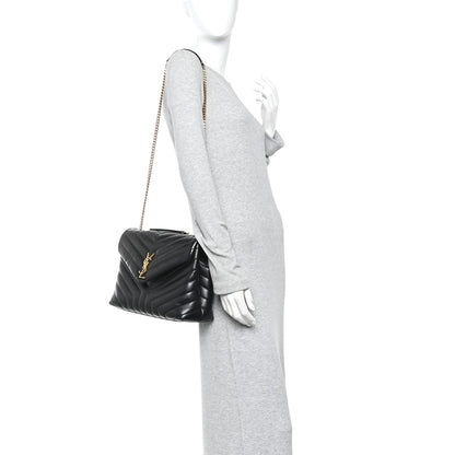 Black quilted satchel with gold chain strap, held at side.
