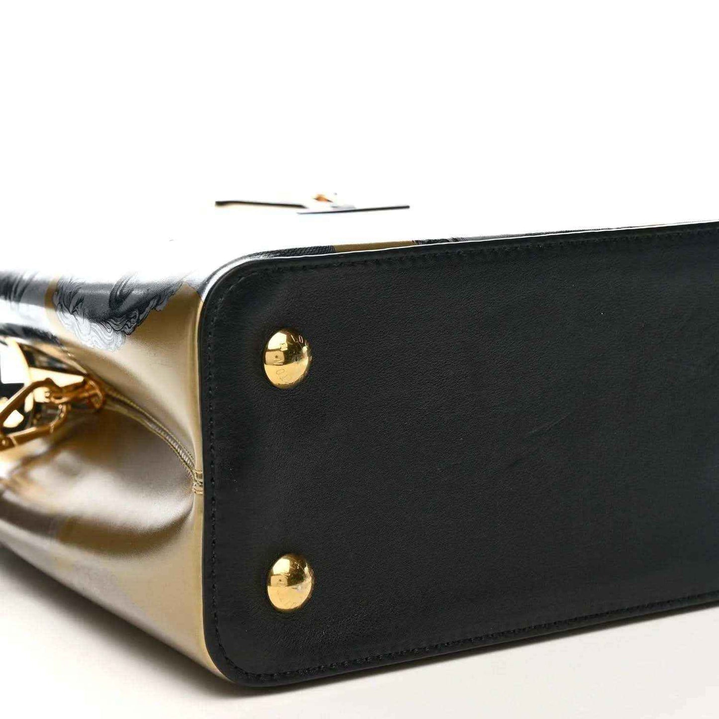 Corner close-up of handbag with gold studs, black leather trim, and silver-gold panel