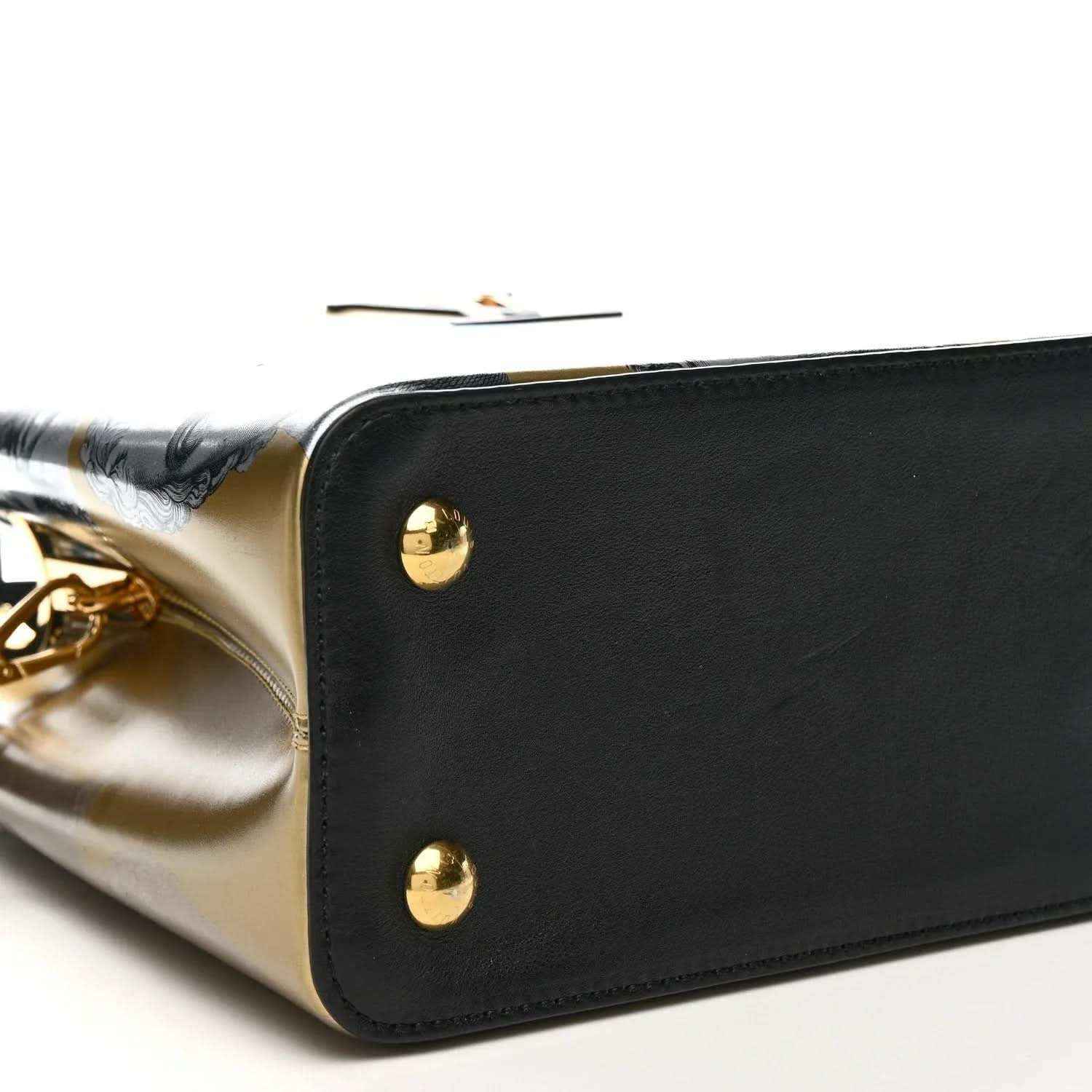 Corner close-up of handbag with gold studs, black leather trim, and silver-gold panel