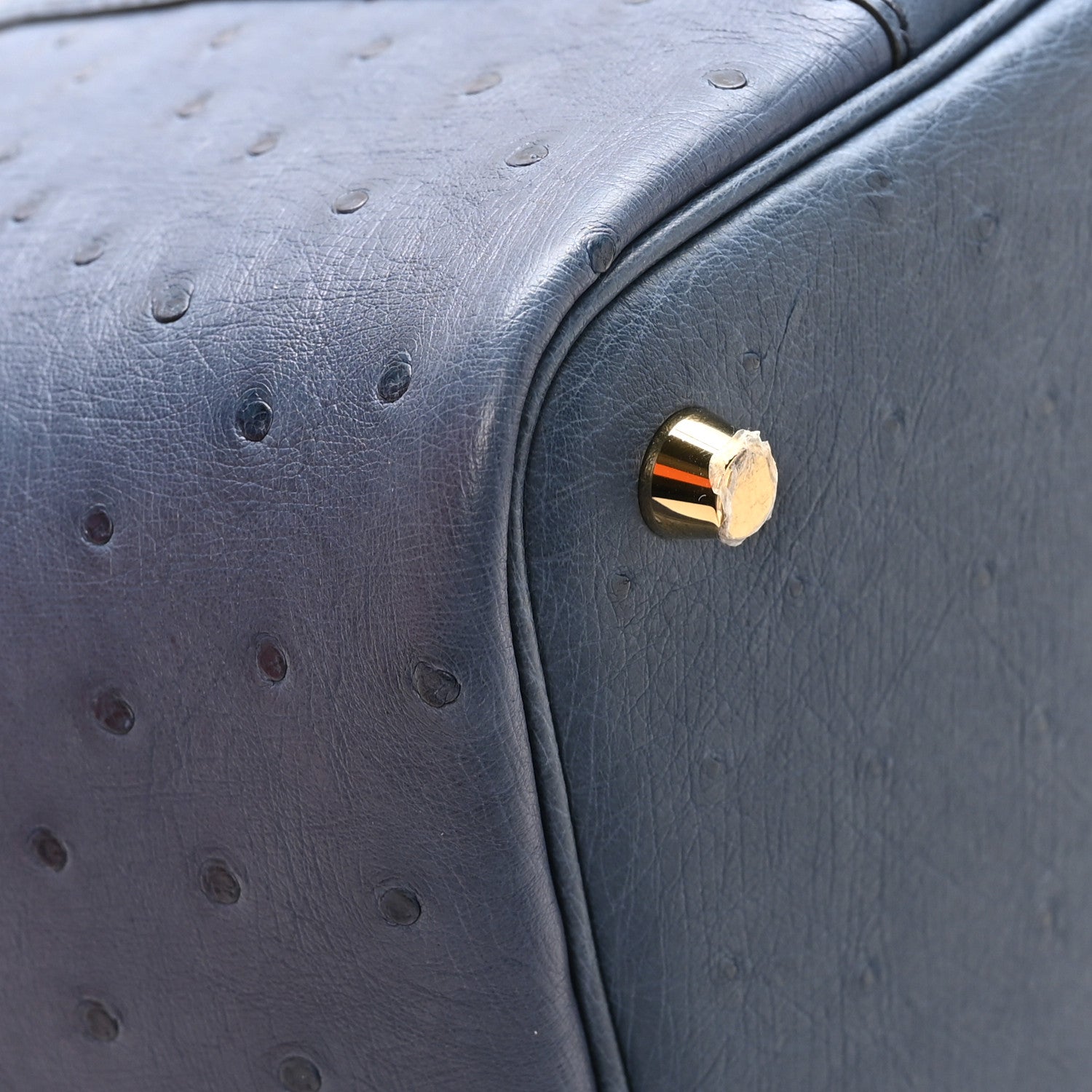 Blue ostrich leather bag corner with round gold-tone clasp hardware.