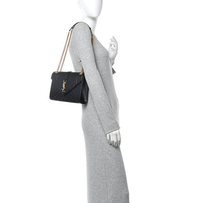 Black leather satchel bag with gold chain shoulder strap worn across the body