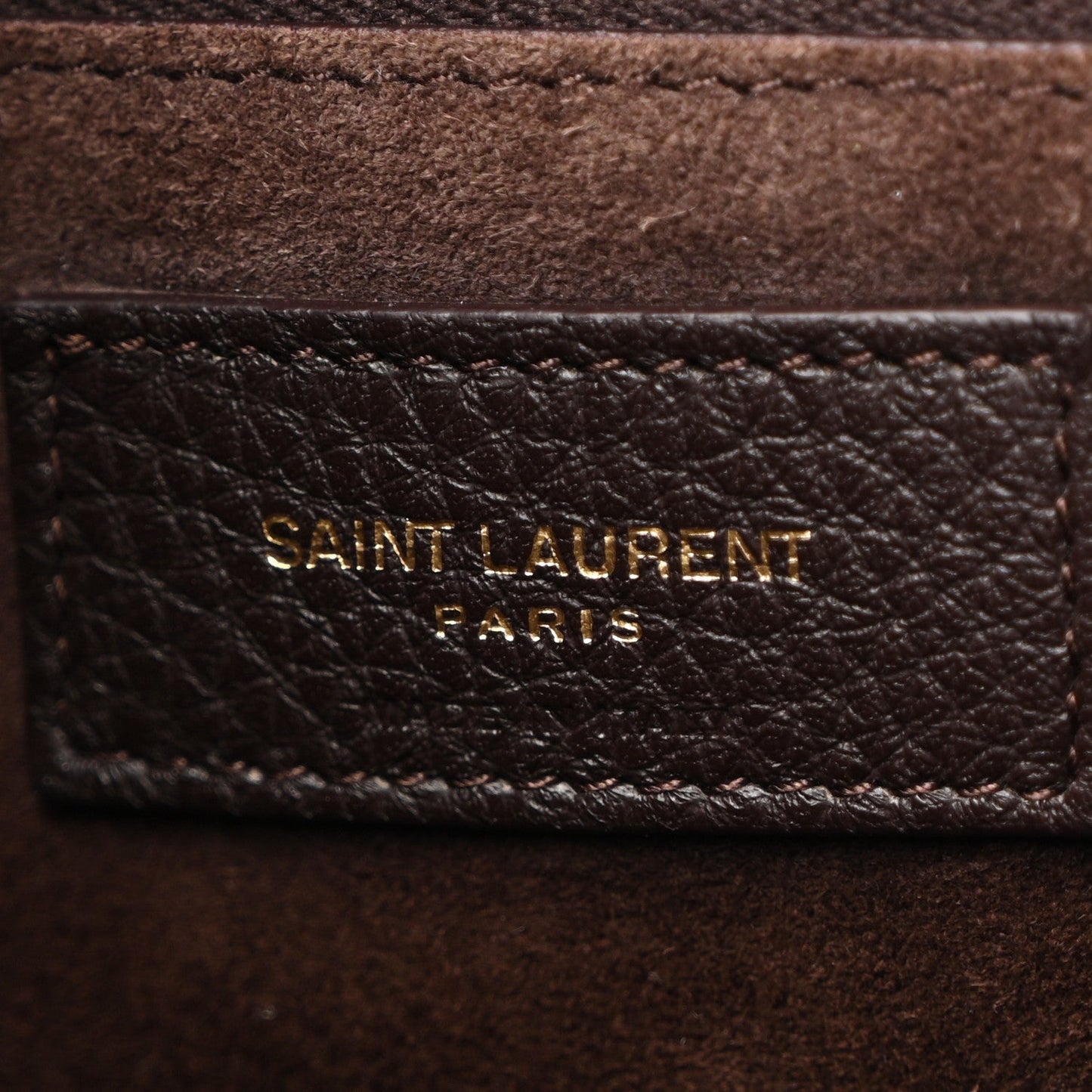 Gold Saint Laurent Paris branding on leather interior panel, dark grained texture