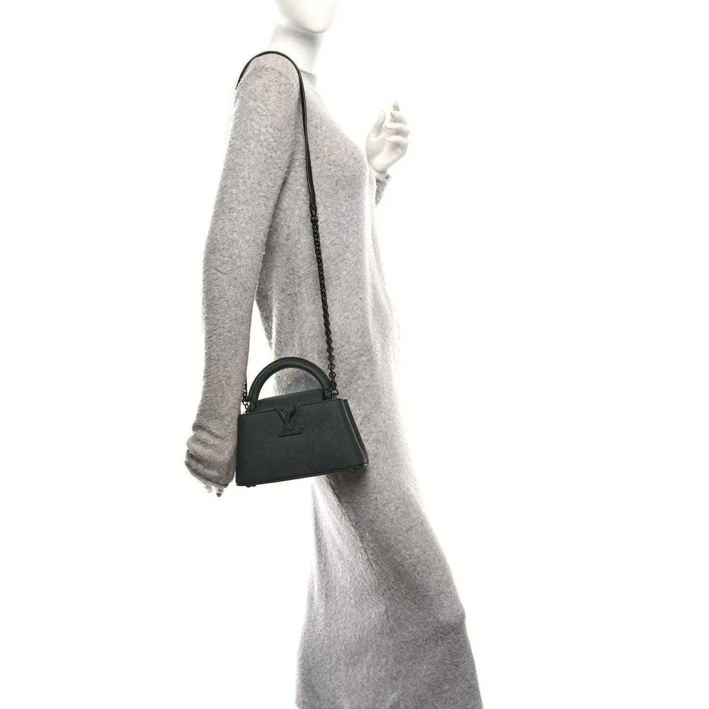 Mini black leather handbag with short handle and crossbody strap, held at side.