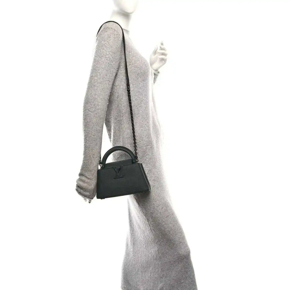 Mini black leather handbag with short handle and crossbody strap, held at side.