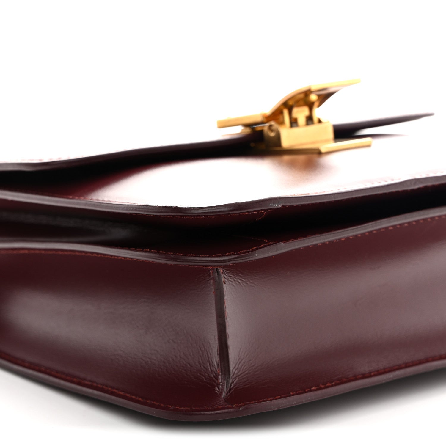 Burgundy leather bag corner with gold-tone clasp and smooth structured fold edges.