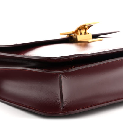 Burgundy leather bag corner with gold-tone clasp and smooth structured fold edges.