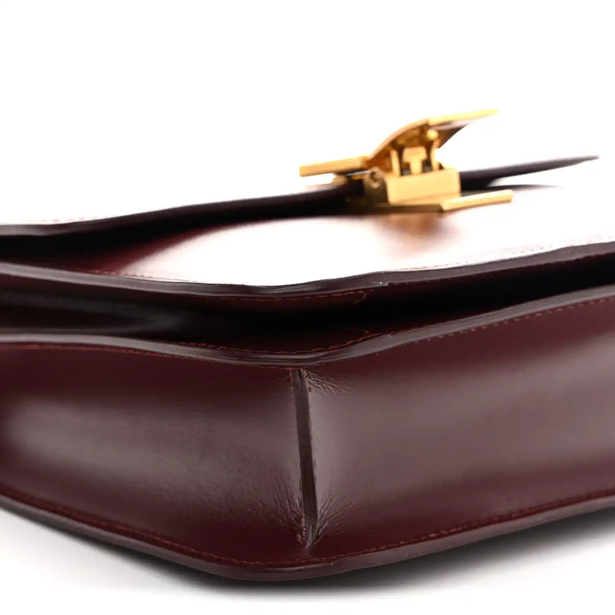 Burgundy leather bag corner with gold-tone clasp and smooth structured fold edges.