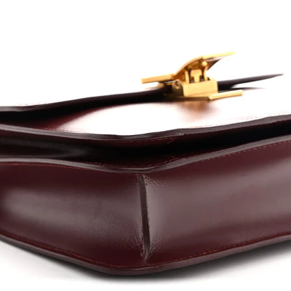 Burgundy leather bag corner with gold-tone clasp and smooth structured fold edges.