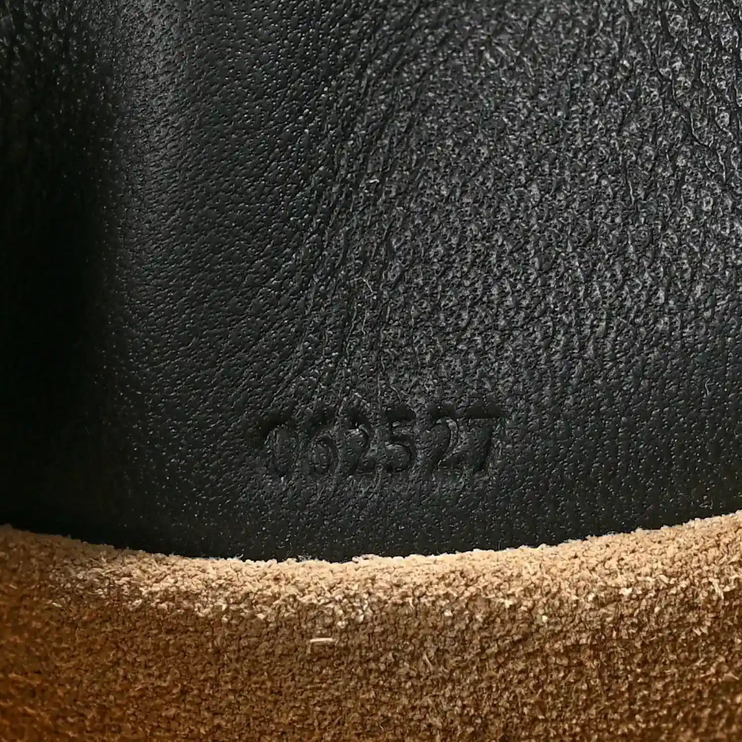 Black leather clutch surface with embossed code marking near the base seam