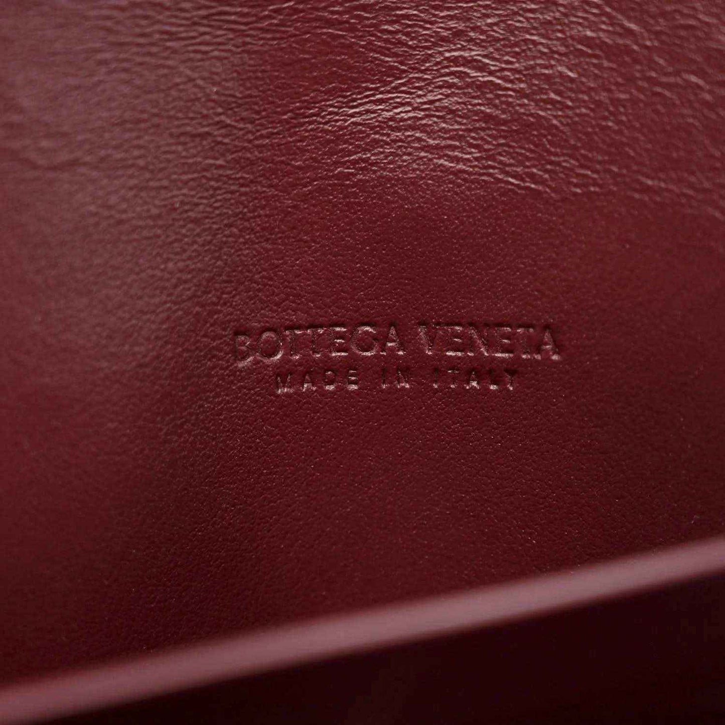 Burgundy leather clutch with embossed Bottega Veneta brand marking on surface
