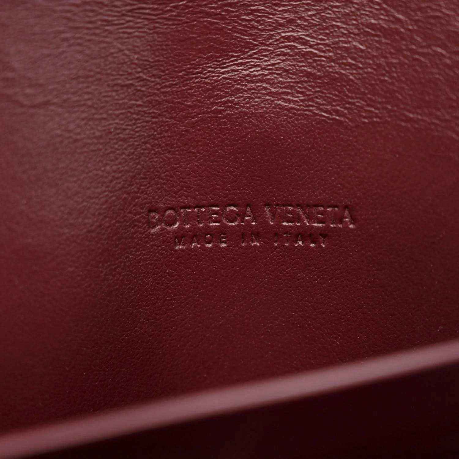 Burgundy leather clutch with embossed Bottega Veneta brand marking on surface