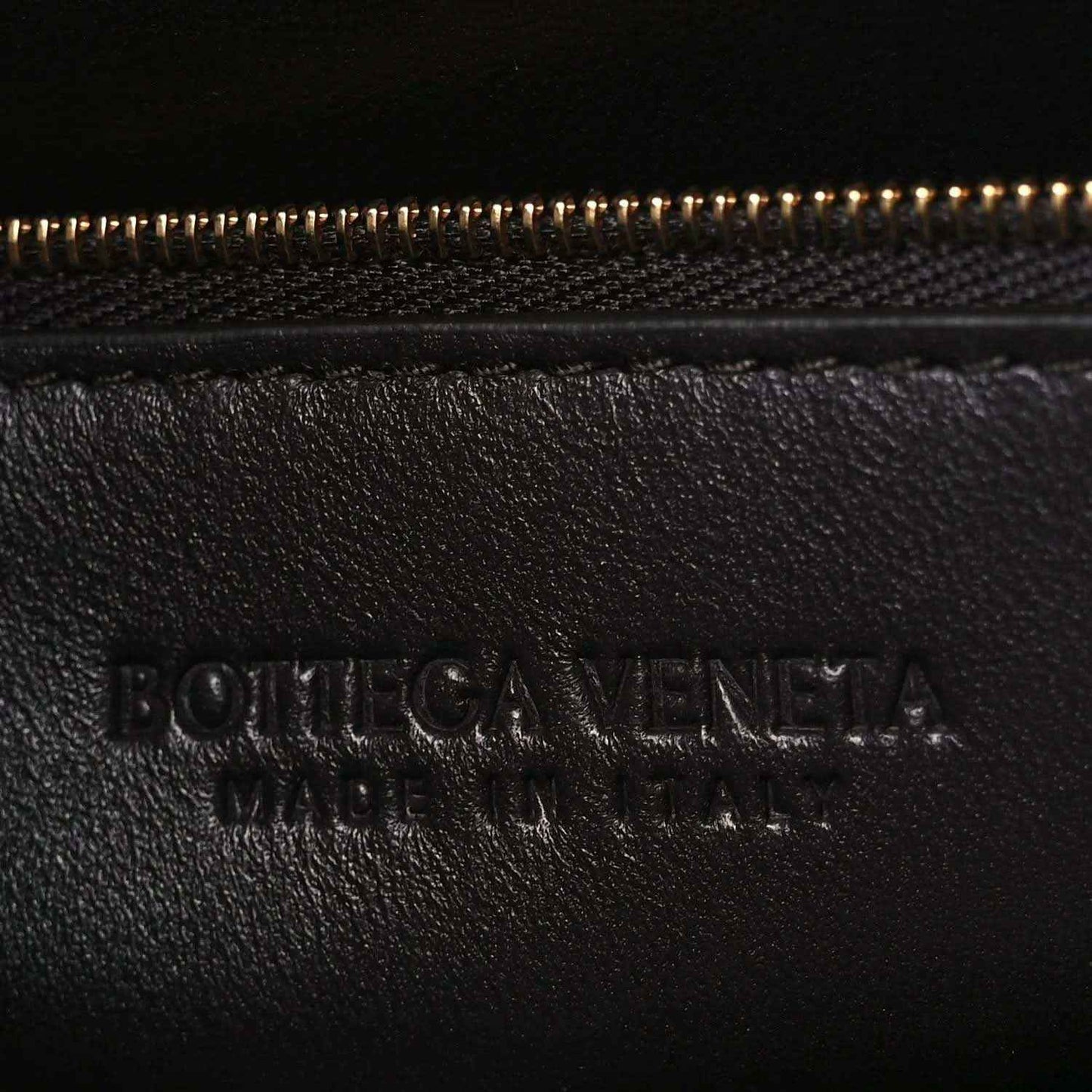 Bottega Veneta embossed logo on dark leather near zipper