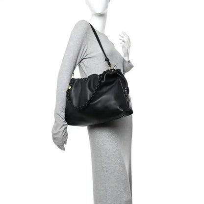 Black leather flamenco bag worn crossbody with drawstring top and chain strap