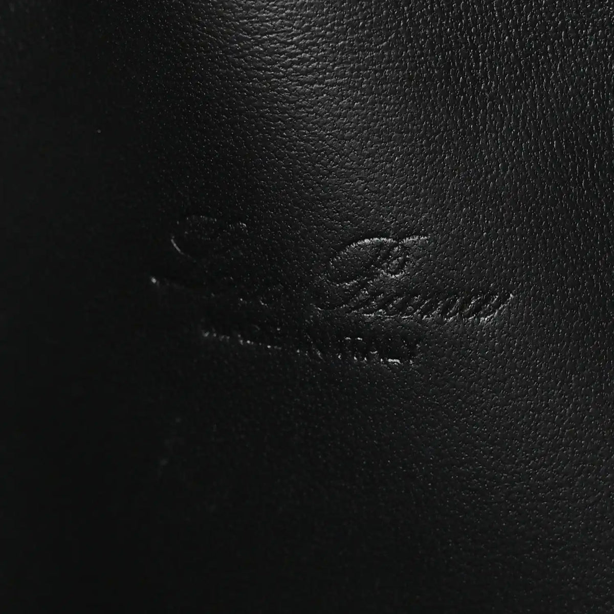 Close-up of black ostrich-textured leather pouch surface with subtle stitching