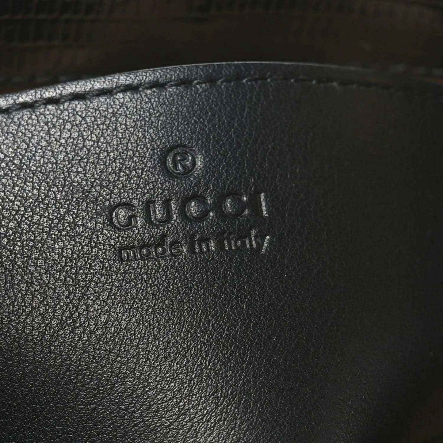 Gucci logo embossed on black leather handbag interior lining.