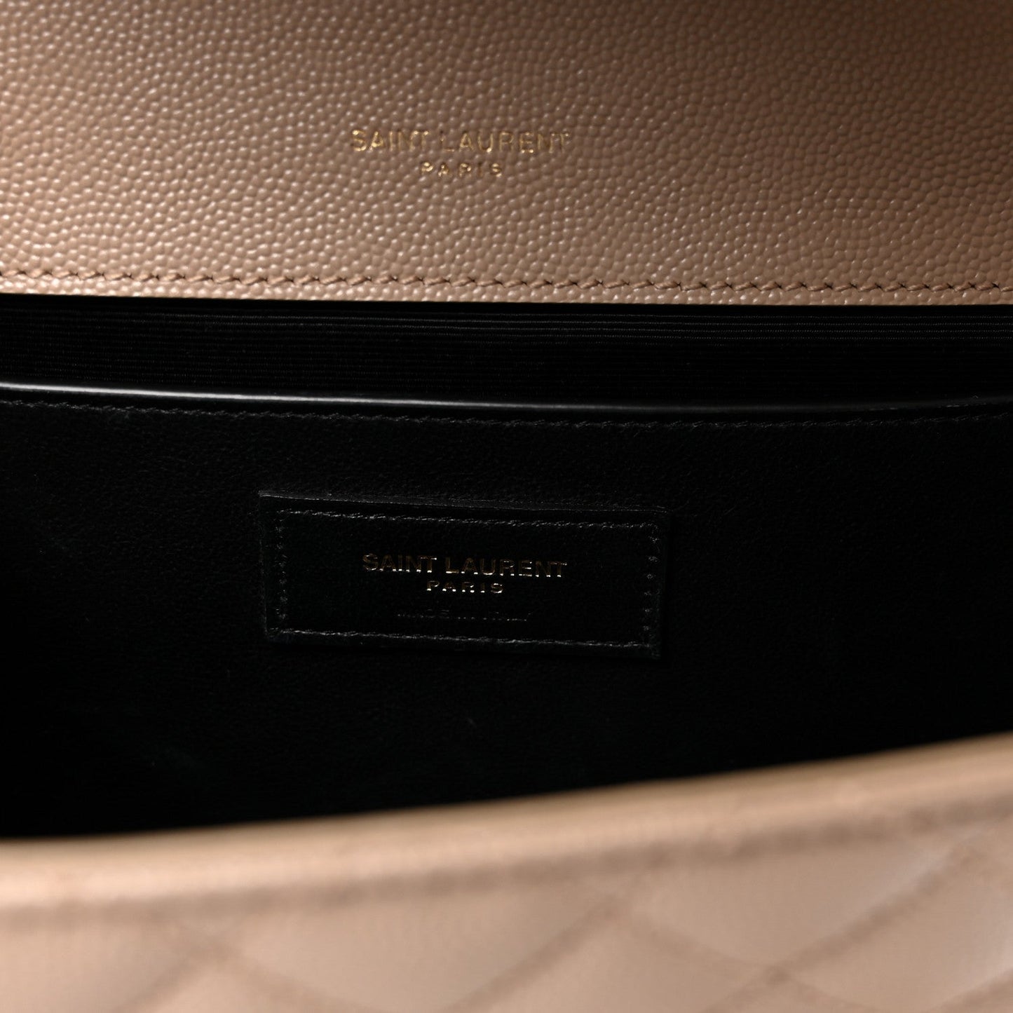 Dark lining interior of satchel with embossed brand patch label in a beige outer frame.
