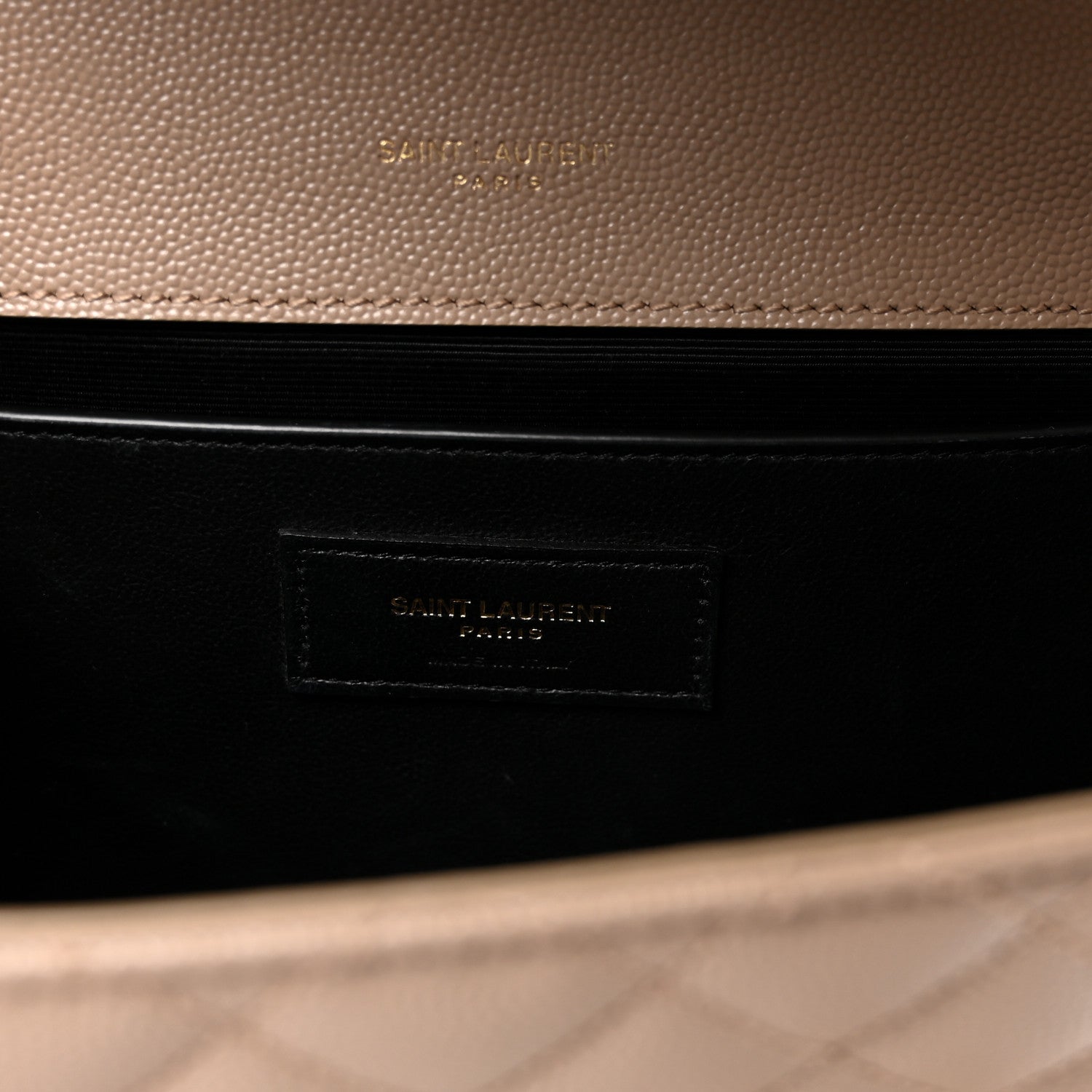 Dark lining interior of satchel with embossed brand patch label in a beige outer frame.