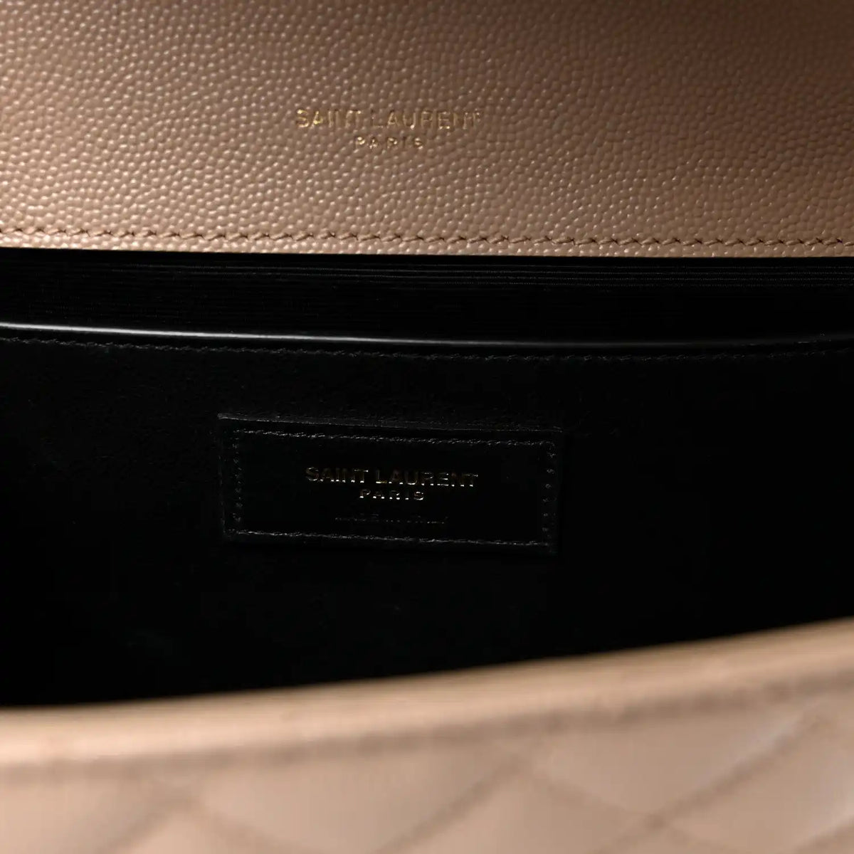 Dark lining interior of satchel with embossed brand patch label in a beige outer frame.