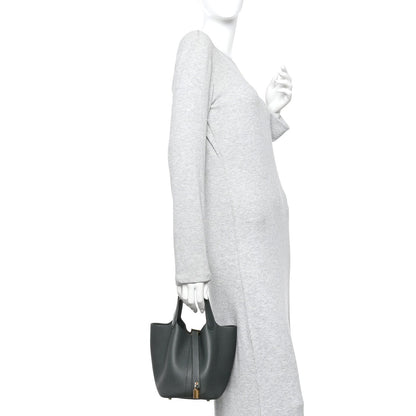 Mini tote bag held at side, textured dark green leather with small gold lock.