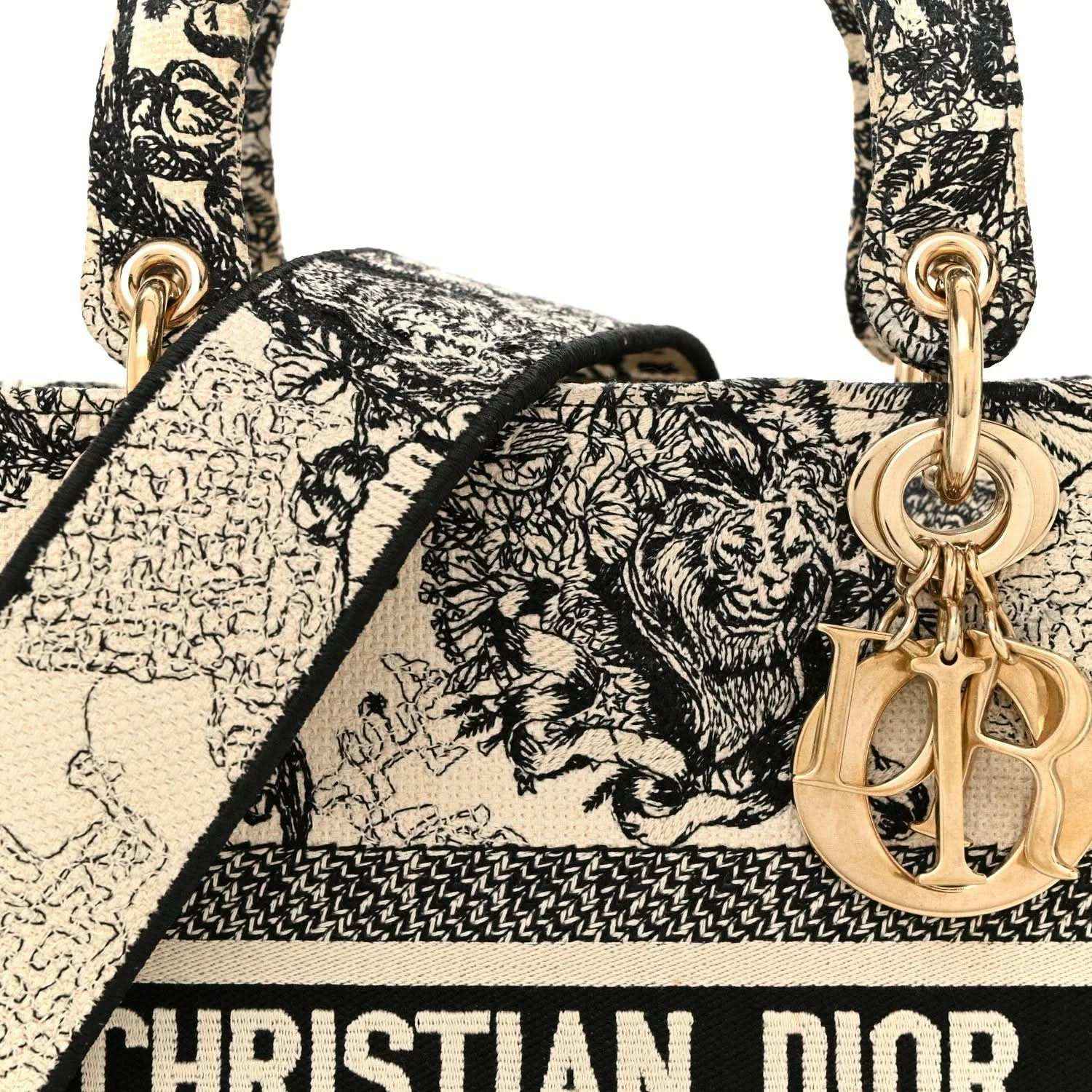 Tote handbag handle area with gold-toned Dior charm and monochrome toile print.