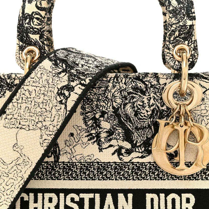 Tote handbag handle area with gold-toned Dior charm and monochrome toile print.