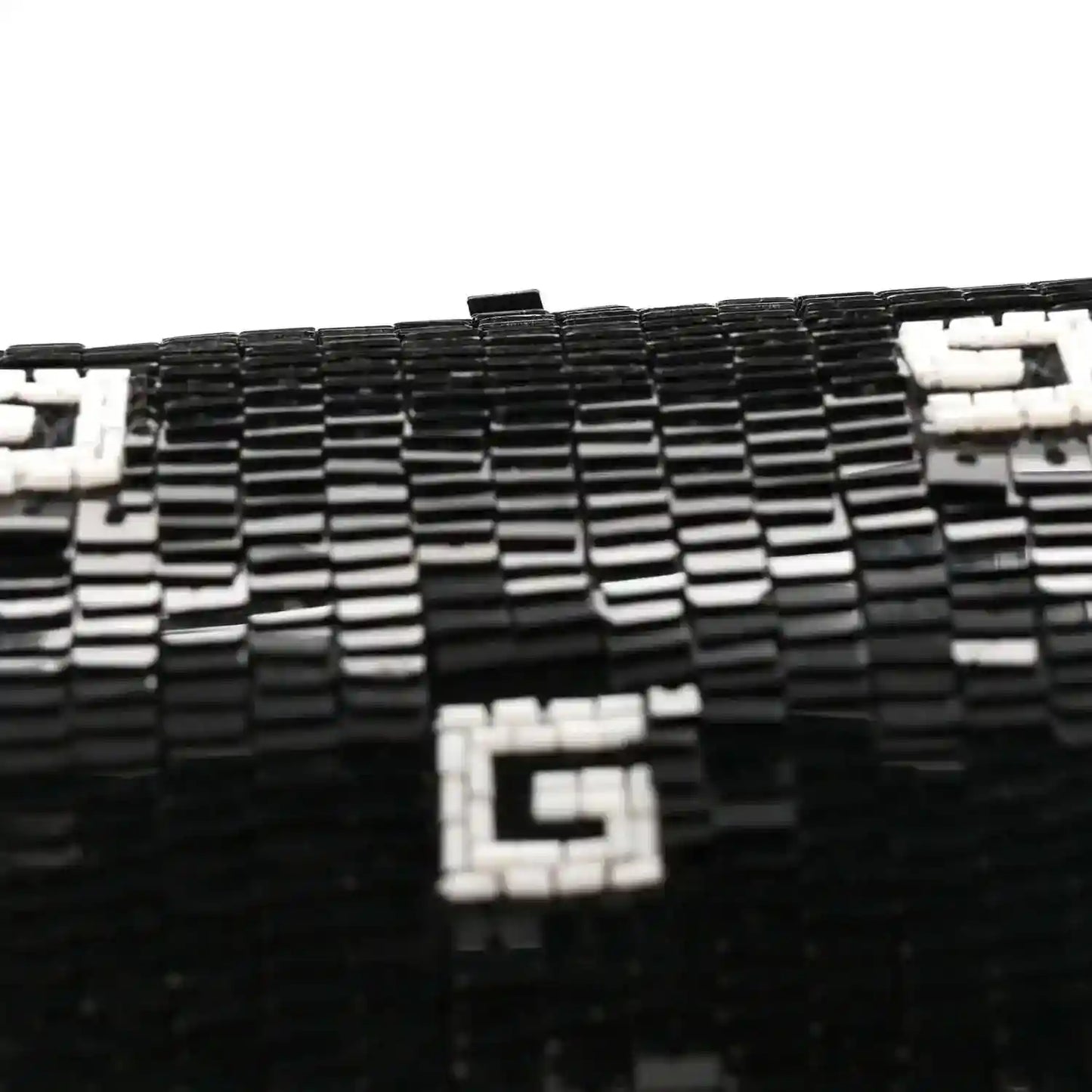 Black mini top handle bag close-up with white square GG motif on textured surface