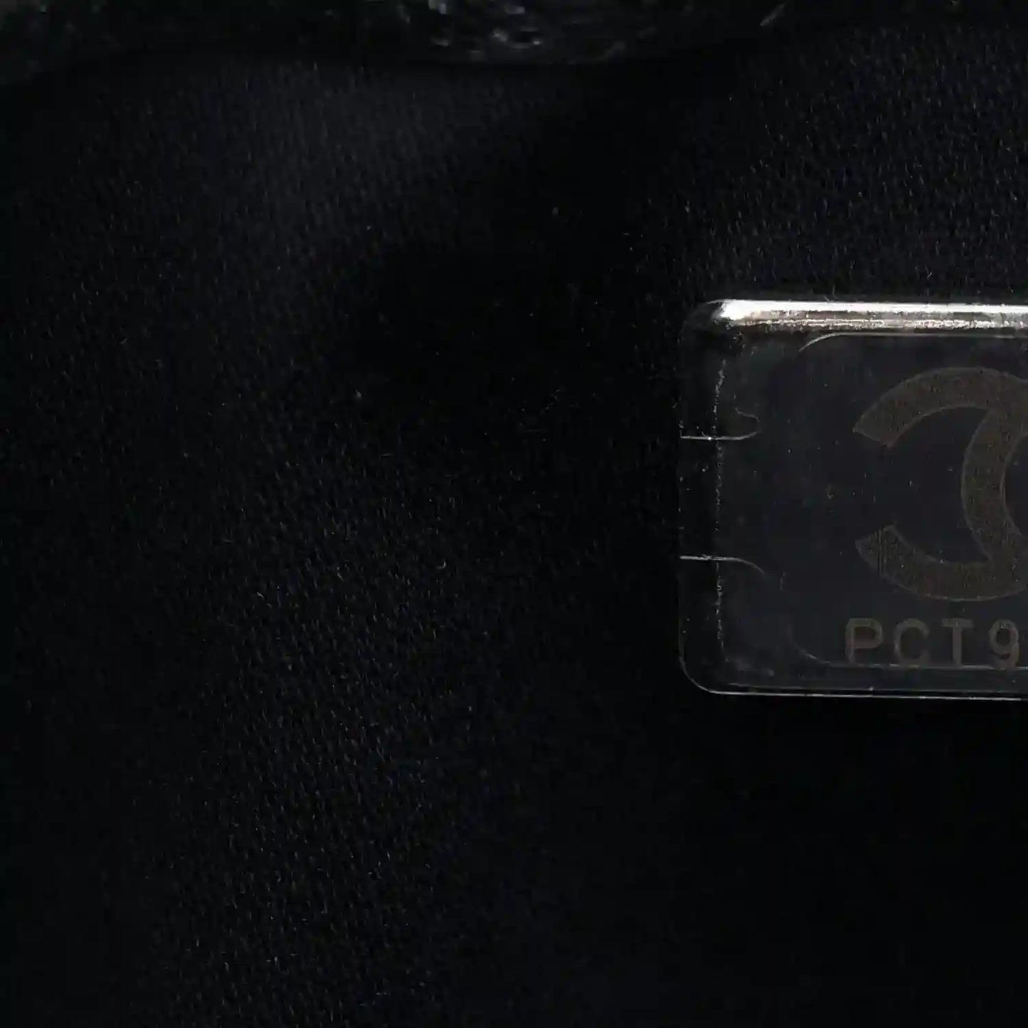 Handbag logo tag detail with metallic hardware on dark quilted caviar leather