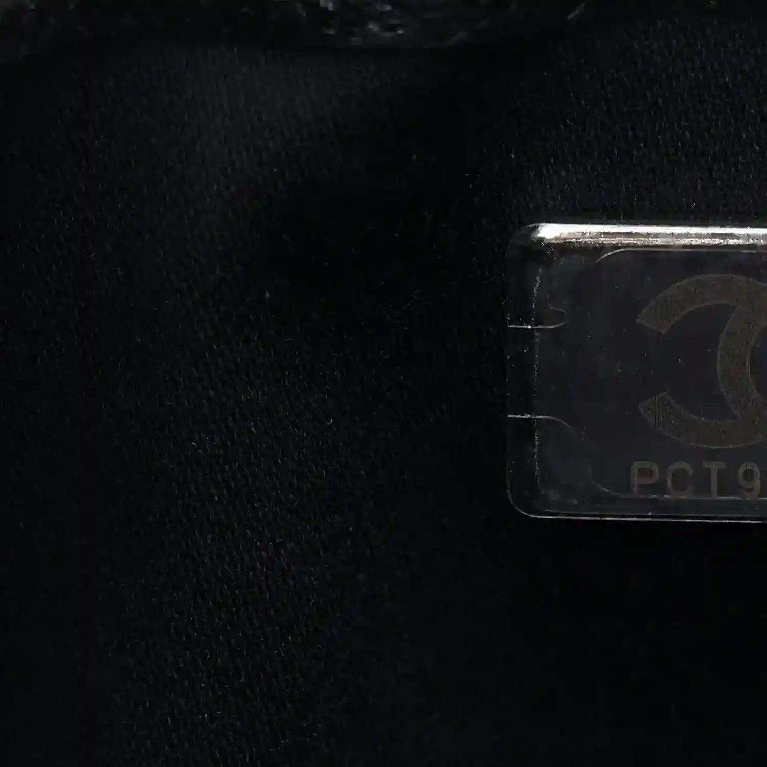 Handbag logo tag detail with metallic hardware on dark quilted caviar leather
