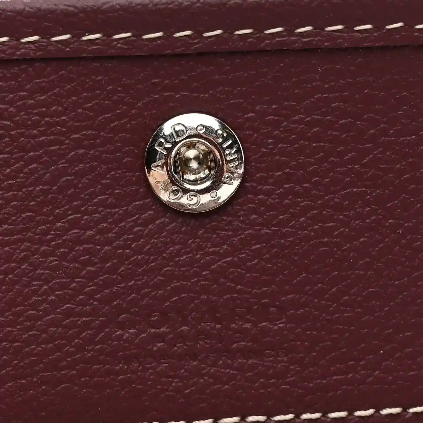 Round silver snap button on burgundy leather flap, with embossed details