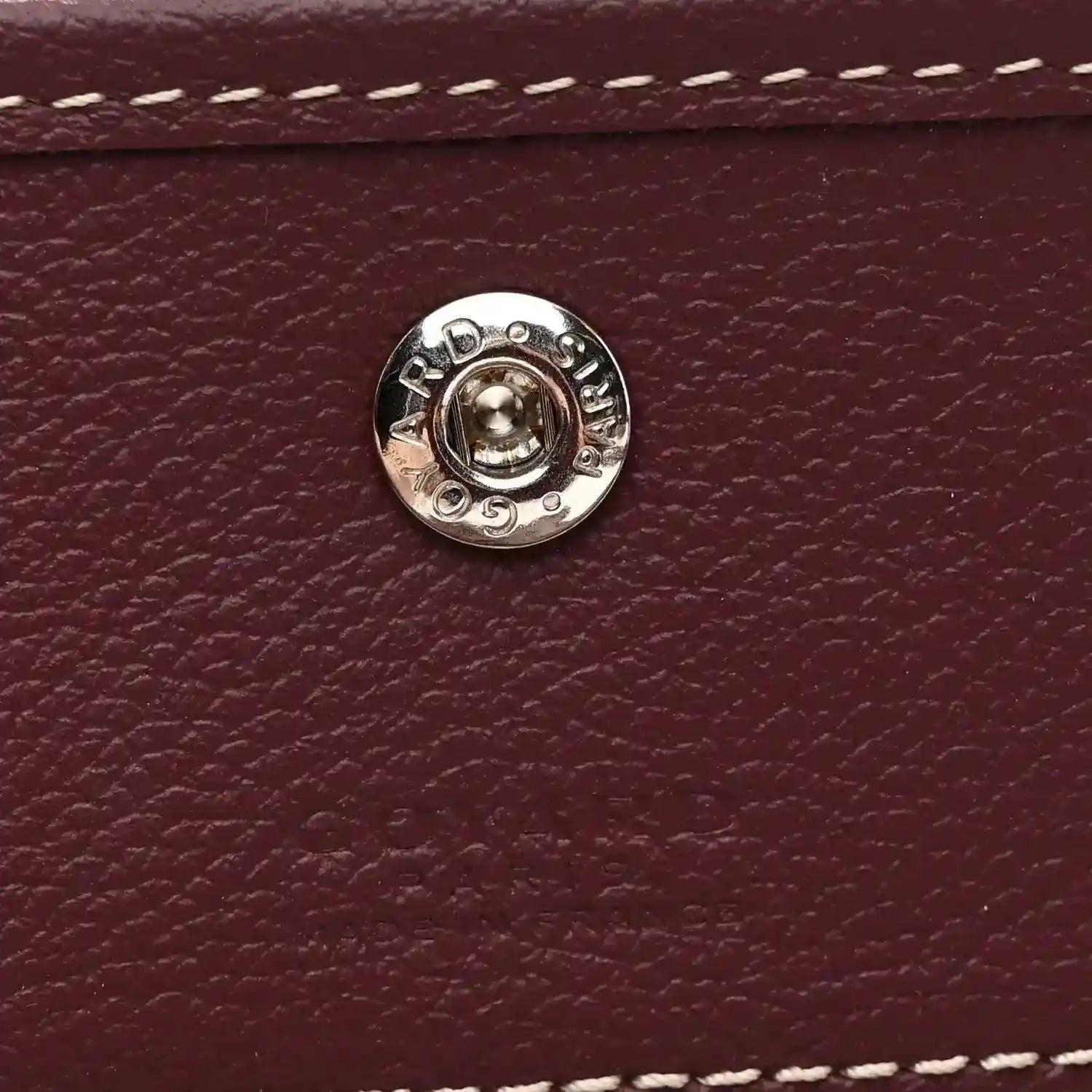 Round silver snap button on burgundy leather flap, with embossed details