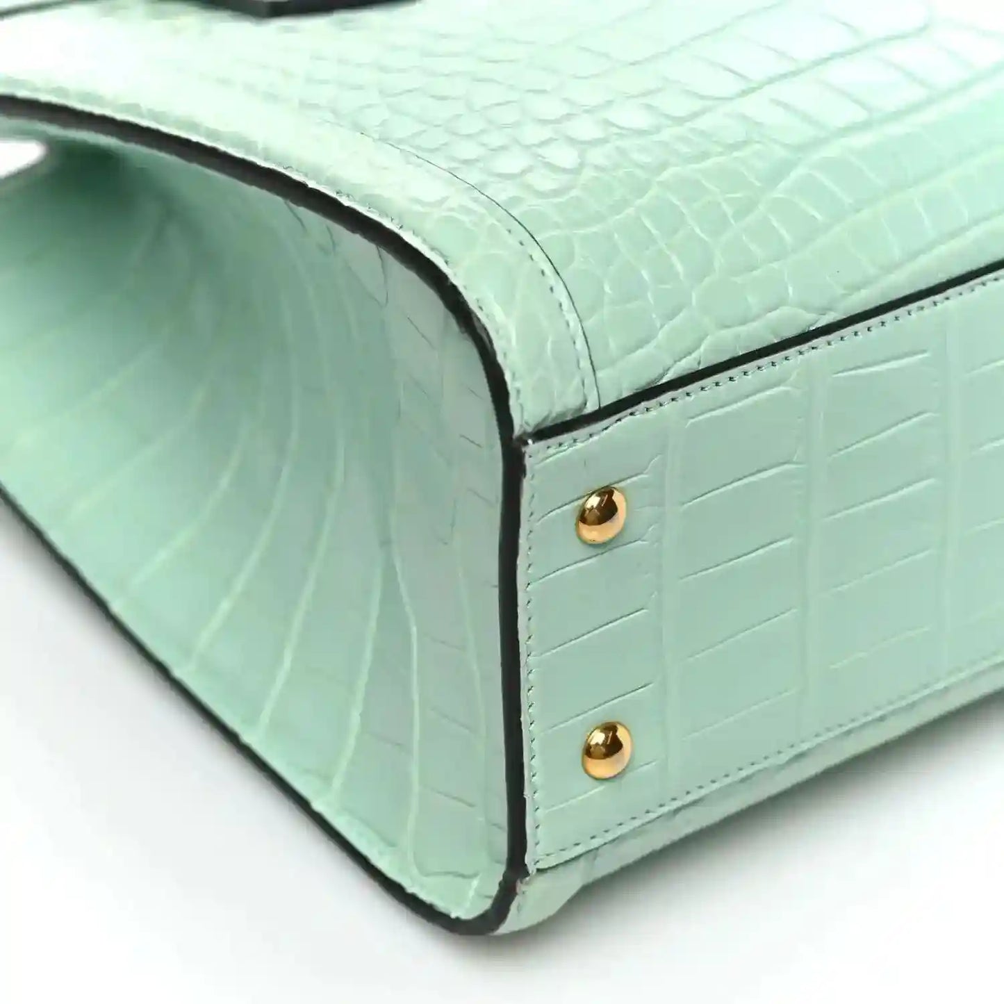 Green alligator-pattern tote bag corner with gold stud hardware and curved base seam