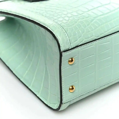 Green alligator-pattern tote bag corner with gold stud hardware and curved base seam