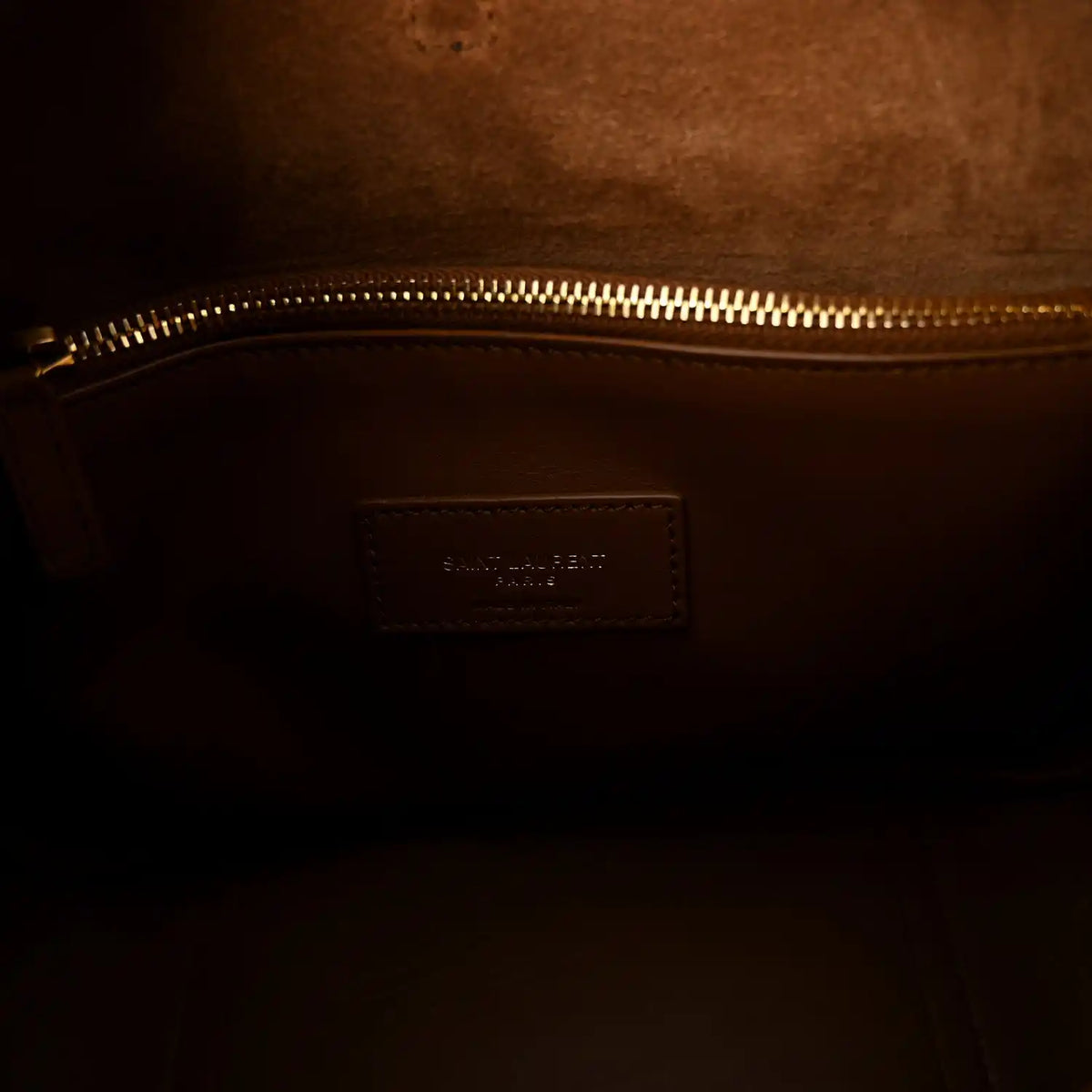Tan leather interior pocket with stitched branding patch near gold zipper