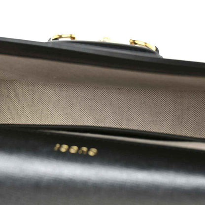 Close-up of black leather flap edge with gold-tone clasp hardware on mini bag