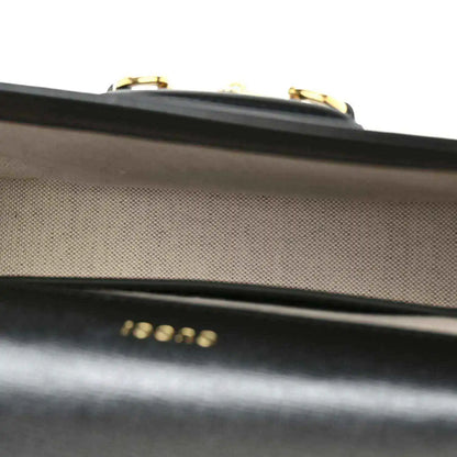 Close-up of black leather flap edge with gold-tone clasp hardware on mini bag