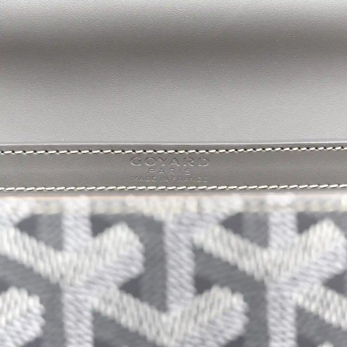 Grey canvas mini Saigon bag close-up of stitched logo emblem on the flap.